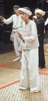 a man in a white shirt and white pants is standing in front of a group of people