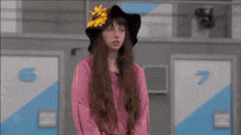 a woman wearing a hat with a sunflower on it stands in front of a wall with the numbers 6 and 7 on it