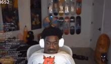 a man wearing headphones and a shirt with a fox on it sits in front of a wall with skateboards on it