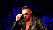 a man wearing sunglasses and a leather jacket stands in front of a crowd