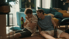 two young men are sitting on the floor drinking wine from bottles