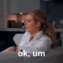 a woman in a white shirt sits on a couch with the words ok um above her