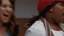 a woman wearing a red hat is laughing with another woman in a white shirt