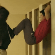 a man in a red shirt hangs upside down on a wall