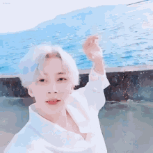 a young boy with white hair is standing in front of the ocean