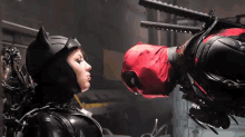 a woman in a catwoman costume kisses a man in a deadpool suit