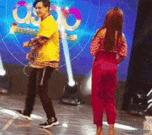a man in a yellow shirt is dancing with a woman in red pants on a stage