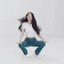 a woman in a white t-shirt and blue jeans is squatting down .