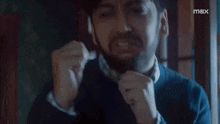 a man is crying while holding his fist to his face in front of a bookshelf .