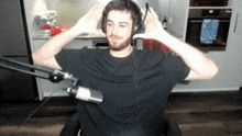 a man wearing headphones and a black shirt is sitting in front of a microphone in a kitchen .