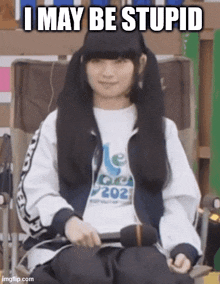 a girl is sitting in a chair with a microphone in her hand and the caption i may be stupid