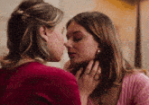 two women are touching each other 's faces and one of them has a ring on her finger