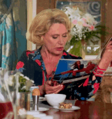 a woman sits at a table reading a magazine with a picture of a woman on it