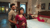 a man and a woman are standing next to each other in a bedroom . the woman is wearing a red saree .