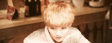 a young man with blonde hair is sitting at a table and making a funny face .