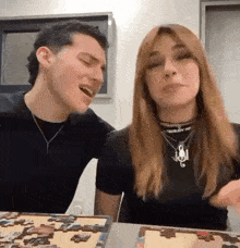 a man and a woman are sitting at a table with a puzzle in front of them and laughing .