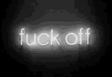 a neon sign that says `` fuck off '' is glowing in the dark on a black background .