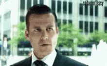 a man in a suit and tie is making a funny face while standing in front of a building .
