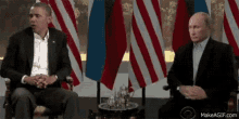 president obama and president putin are sitting in front of flags .