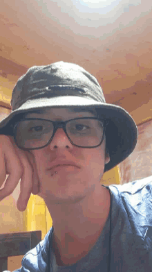 a man wearing a hat and glasses holds his hand to his chin