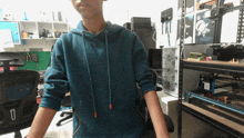 a man in a blue hoodie is standing in a room with a shelf that says ' a ' on it