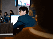 a man wearing glasses sits at a desk in front of a computer