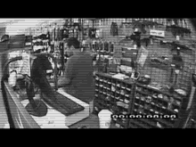a black and white photo of a man sitting at a counter in a shop .