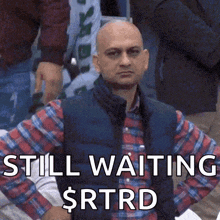 a bald man in a plaid shirt is sitting in a crowd and says still waiting $ rtrd