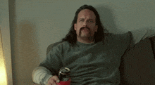 a man with long hair and a mustache is sitting on a couch holding a can of diet coke and says no
