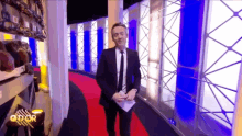 a man in a suit and tie is standing on a red carpet in front of a sign that says q'dor