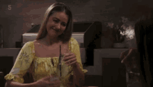 a woman in a yellow floral top holds a can of soda
