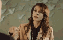 a woman in a suit and pearl necklace is talking to a man in a suit .