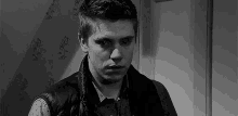 a black and white photo of a young man wearing a vest and a scarf .
