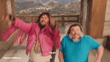a man in a pink jacket is standing next to another man in a blue shirt and says yeah