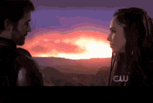 a man and a woman are looking at each other in front of a sunset with the letters cw on the bottom