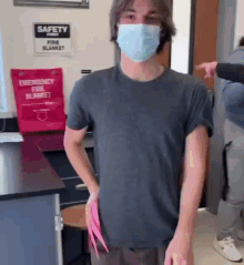 a man wearing a face mask is standing in front of a sign that says safety fire blanket .