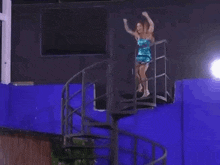 a woman in a blue dress is standing on a set of spiral stairs .