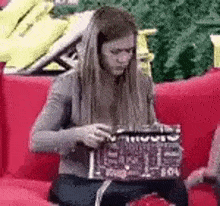 a woman is sitting on a red couch holding a laptop .