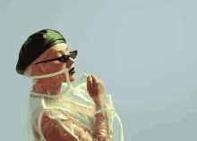 a woman wearing a green hat and sunglasses is standing in a clear plastic coat