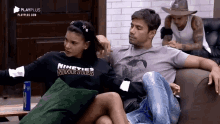 a man and a woman are sitting on a couch and the woman is wearing a nineties nineties sweatshirt