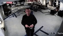 a man in a black shirt is standing in a room with the time of 09:14:23 on the screen