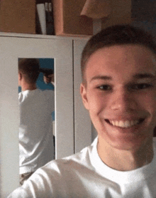 a young man is smiling in front of a mirror while another man holds a gun to his head