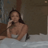a woman is sitting on a bed talking on a telephone