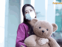 a woman wearing a mask holds a teddy bear in front of a news sign