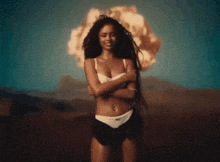 a woman in a bikini is standing in front of an explosion in the desert