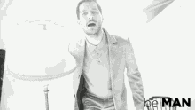 a man in a suit and tie is standing in front of a lamp .