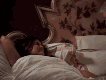 a woman is laying on a bed with white sheets and a floral headboard