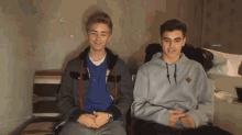 two young men are sitting next to each other and one has a gray hoodie on