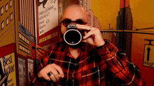 a man in a plaid shirt is taking a picture of himself in front of a poster for thriller movie gun bullet