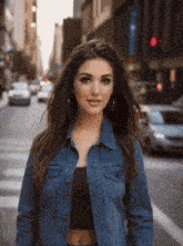 a woman wearing a denim jacket is standing on a street